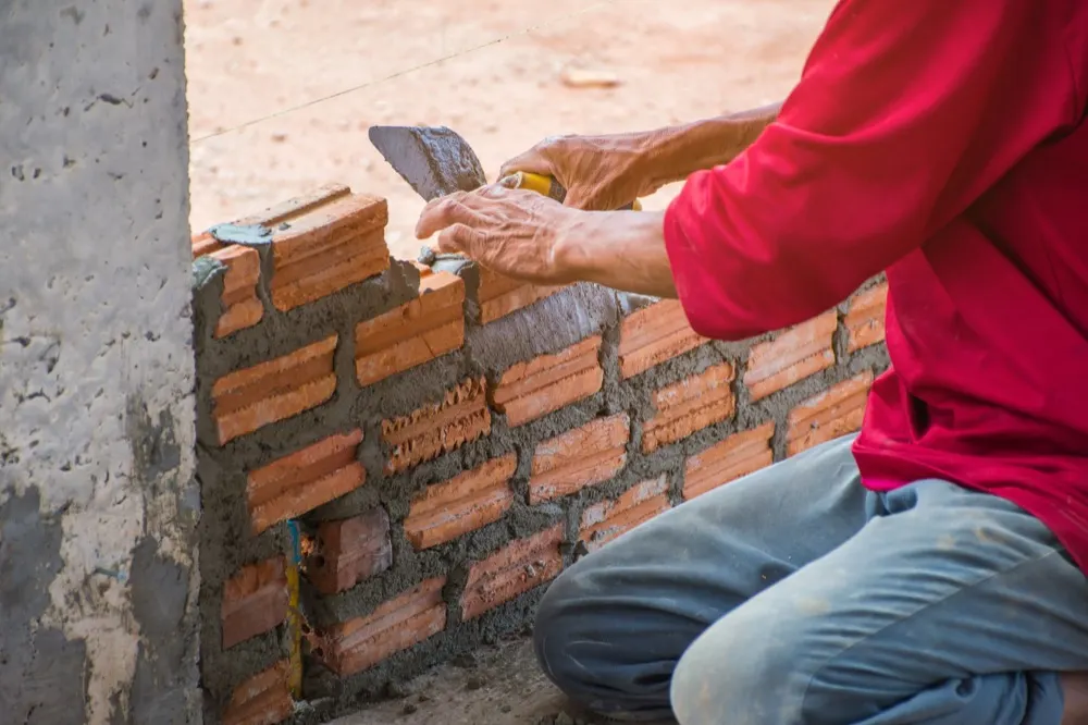 A bricklayer laying bricks with a trowel, working to a string line.