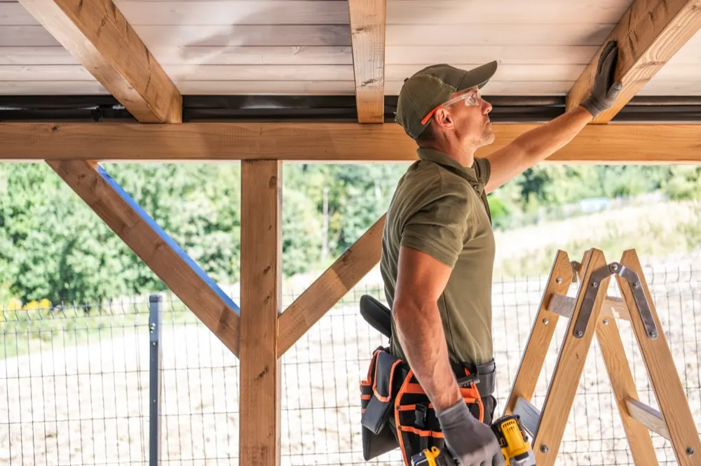 A builder in a tool belt working overhead on a timber frame.