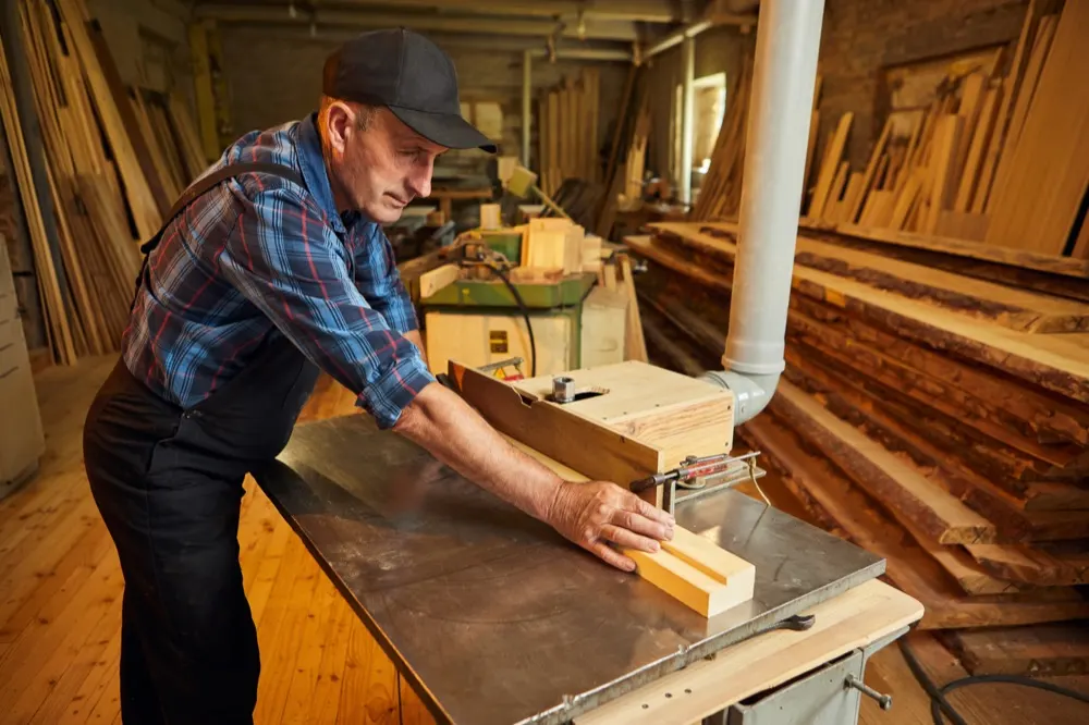 A carpenter feeding a length of timber through a bench saw in a workshop.