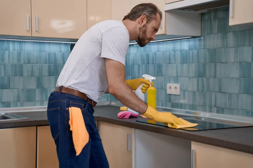 A cleaner wiping down a hob in a domestic kitchen.