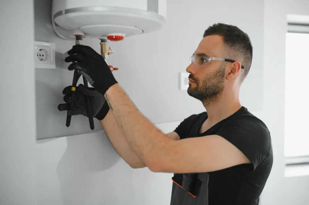 A heating engineer in safety glasses working on a wall-mounted boiler.