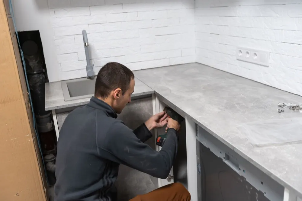 A kitchen fitter fixing a base unit with a cordless drill, worktop already in.